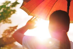 Girl holding an umbrella and raising her hand to block hot sunlight.